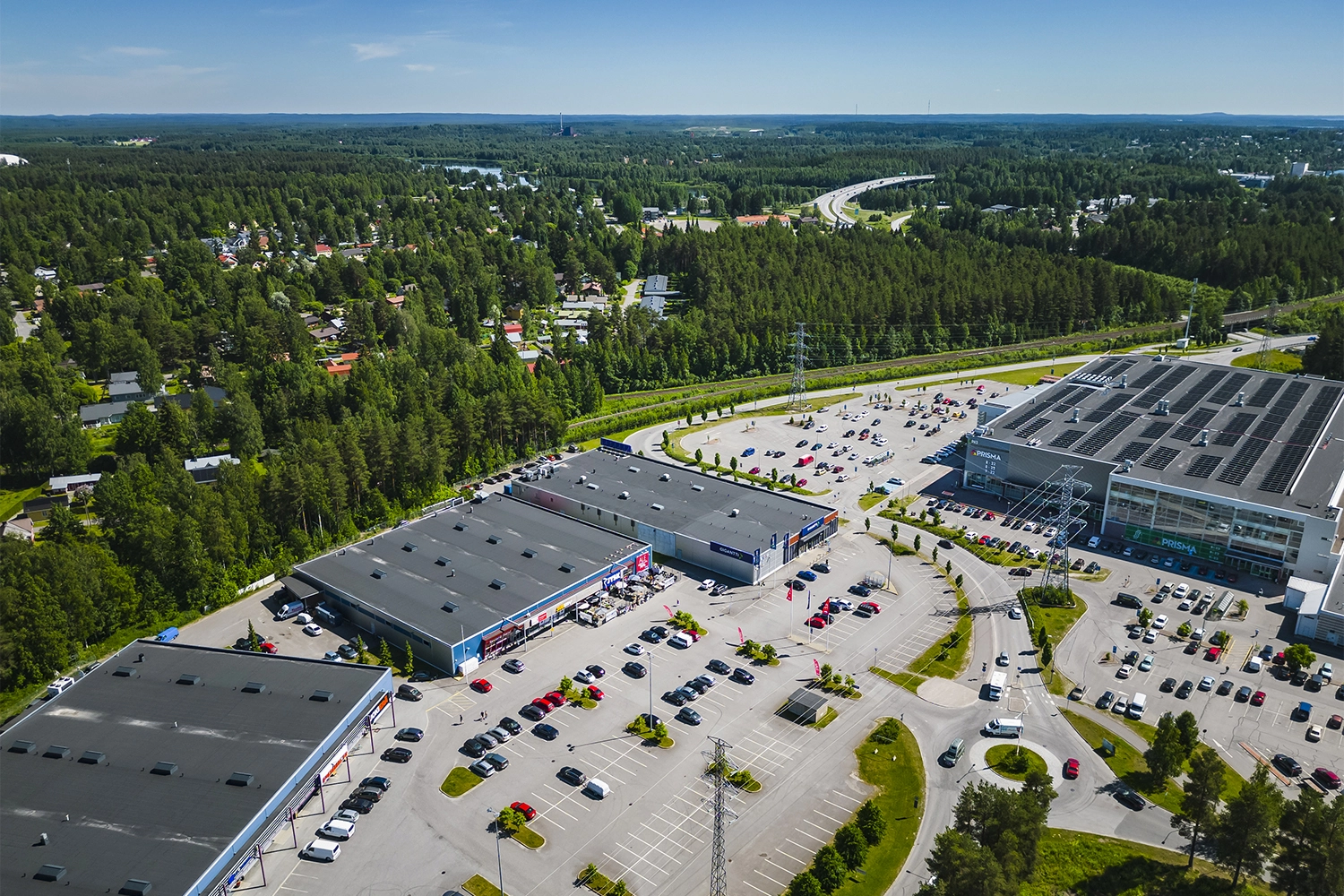 Joensuun Voimatie 10 harmaa kattoinen liikekiinteistö, jonka ympärillä tilavat pysäköintialueet. Takana metsämaisema.