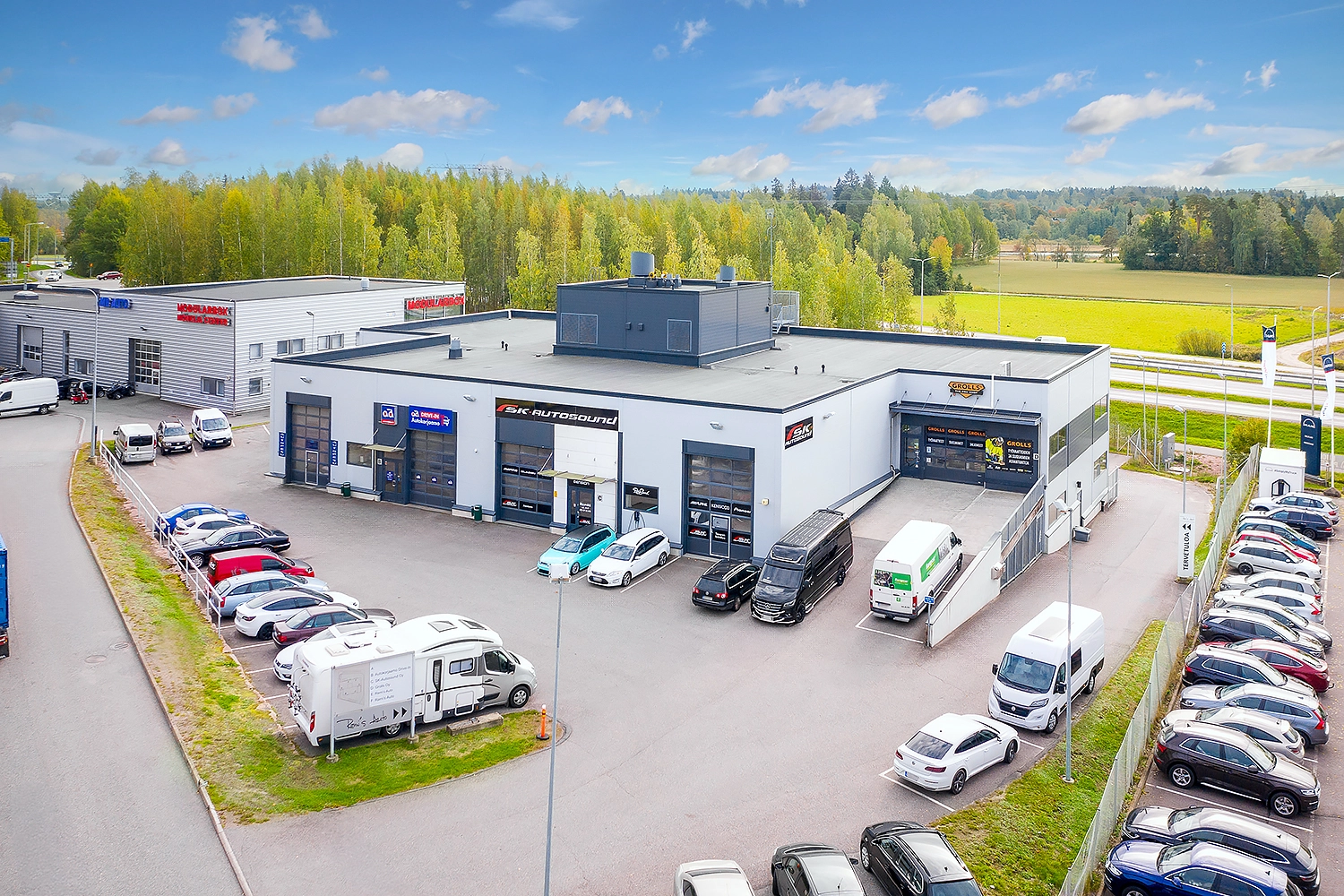 Liikekiinteistöstä Espoon Kartanonherrantie 7:ssä, jossa toimii useita auto- ja konealan yrityksiä. Kiinteistön edessä autoja pysäköitynä parkkialueelle.
