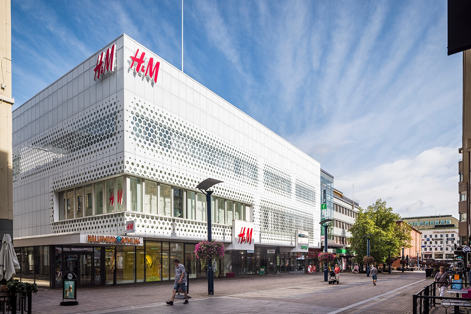 Jyväskylän Kauppakatu 37 valkoinen julkisivu, jossa suuret H&M-valokyltit. Katutasossa korkeat ikkunat, ylemmissä kerroksissa rei'itetyt varjostukset. 