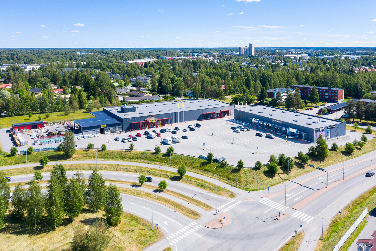 Kahdesta laatikkomaisesta liikerakennksesta koostuva Seinäjoen Päivölänkatu 2 ilmakuvassa, edessä iso pysäköintialue ja tien liittymä. 