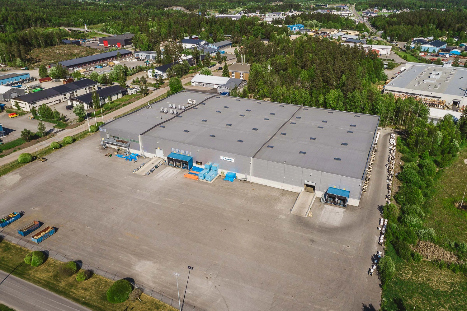 Kaarinan Asessorinkatu 3, ilmakuva. Kiinteistön julkisivu on harmaa, seinällä on neljä lastaustaskua ja kaksi ovea joista pääsee ajamaan autolla sisään. Edustalla paljon tilaa, taustalla metsikköä.