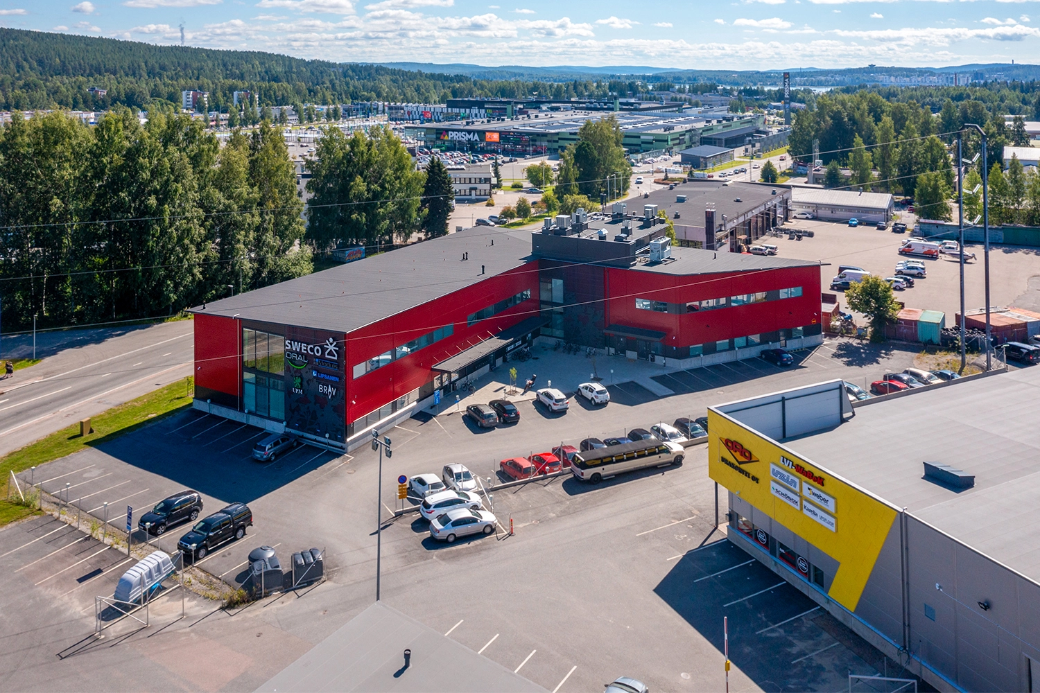 Jyväskylän Vasarakatu 23 A ilmakuvassa. Punainen kaksikerroksinen liike/toimistorakennus sijaitsee kaupallisella alueella, pihassa pysäköintitilaa.