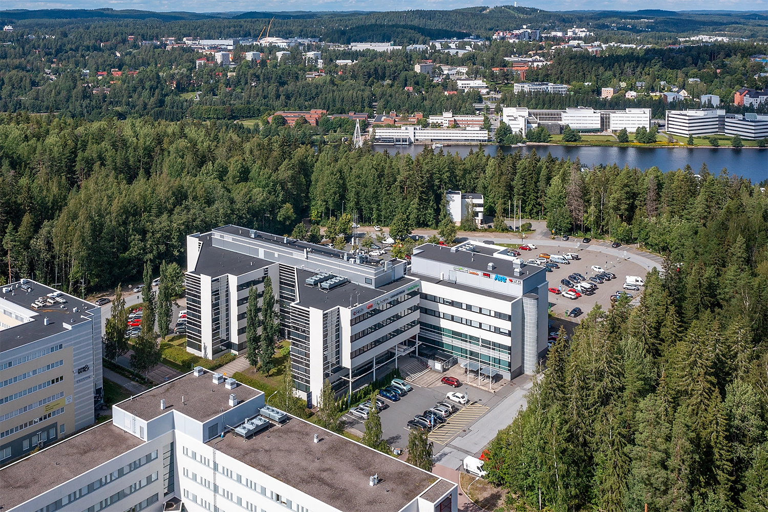 Ilmakuvassa Jyväskylän Ohjelmakaari 2&10, joka on kahdesta toisiinsa yhdistyvästä toimistorakennuksesta muodostuva toimitilakokonaisuus. Taustalla näkyy metsää ja Mattilanniemen rakennuksia...